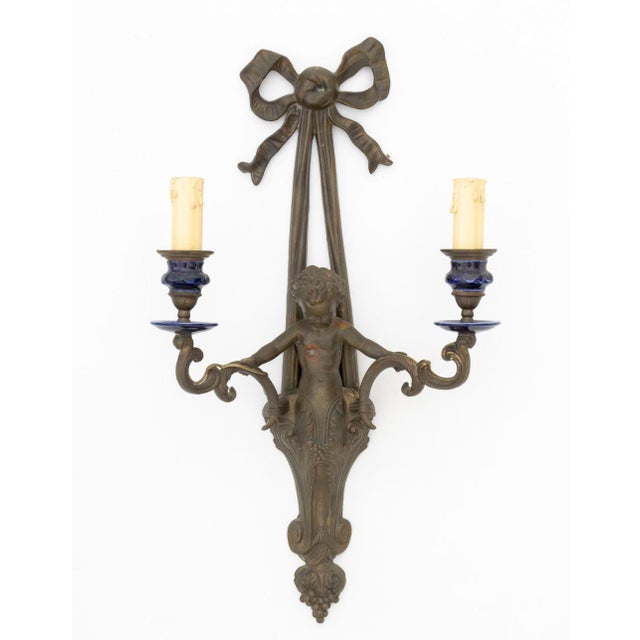 Pair of Patinated Brass Cherub Candlestick Wall Sconces, two arms with blue ceramic candle base, with ribbon bow top. 22"...