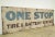 Reclaimed movie set sign made of aluminum in brown, tan, blue, red, and black colors. The sign reads "One Stop, Tire &...