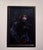 Magique Noir presents a figure enveloped in shadow, their striking red and white face paint contrasting sharply with the...