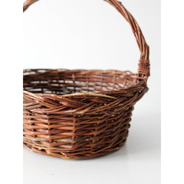 A vintage handwoven wicker gathering basket with a gracefully arched handle and timeless, rustic appeal. Beautifully woven...