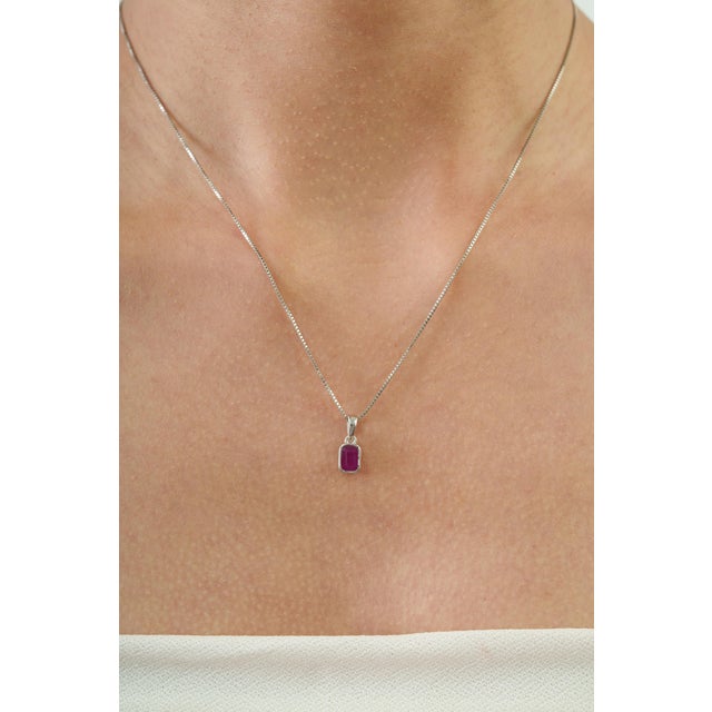 The Minimalist Cushion Cut Natural Red Ruby Bezel-Set Solitaire Pendant, designed by Carat&Her, features a beautiful...