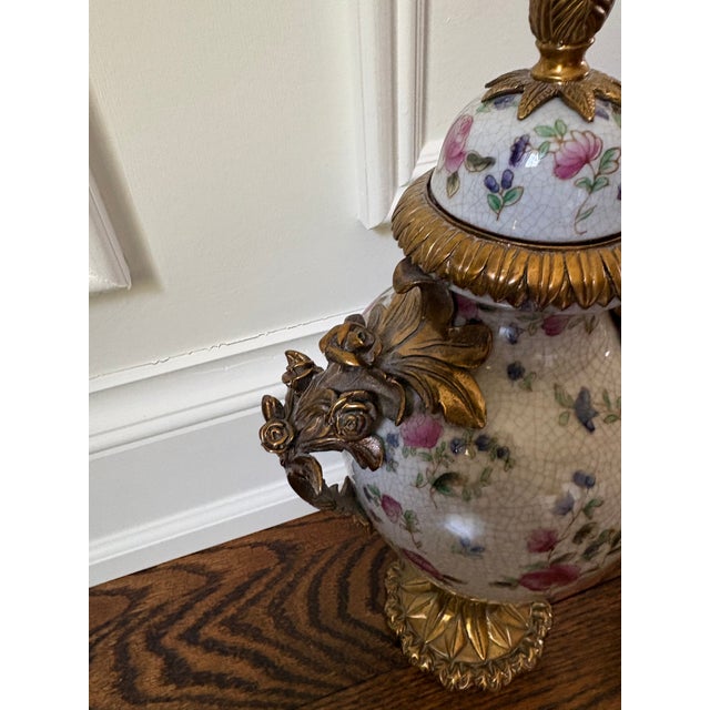 Porcelain covered urn with ornate bronze handles, base and trim. Features a crackled glaze finish with hand-painted pink...