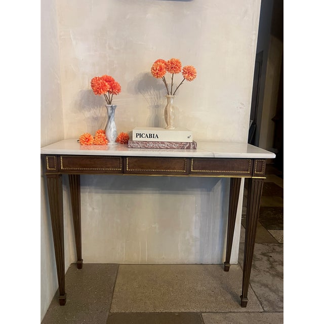 Mahogany wood console table with inlaid brass accents and trim. There is a natural fissure in the marble that is supported...