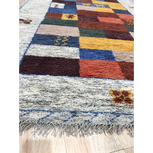 A 6' x 9' hand-knotted wool rug with a Gabbeh-style patchwork of red, blue, gold and brown blocks with small animal motifs...