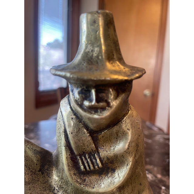 Brass Sculpture of Seated Man (milagro rancher), all bundled up with scarf and hat. Sits on a wood base which measures 2...