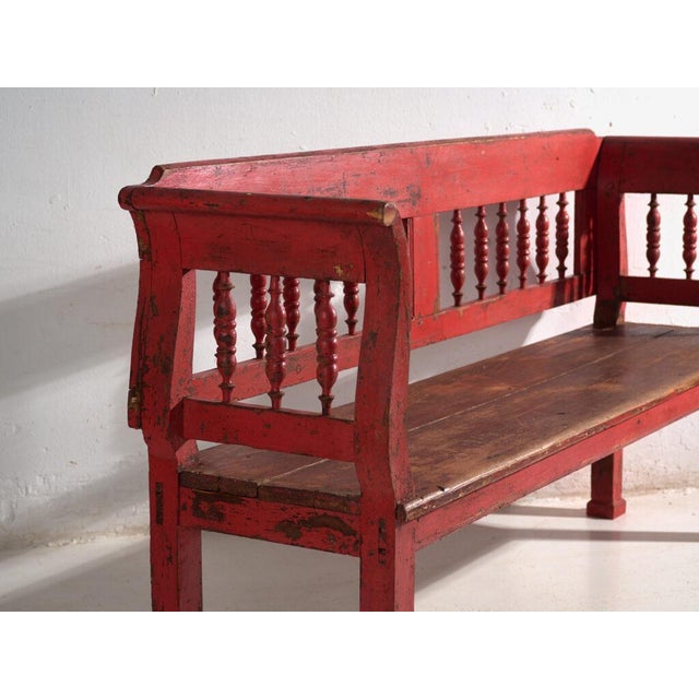 This antique red painted bench in pine wood is a bench with a backrest of turned spindles and armrests, with a continuous...