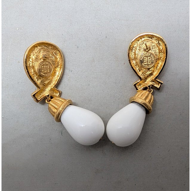 1980s goldtone tear drop white cabochon rhinestone top with textured goldtone loop surround with white resin drop with...