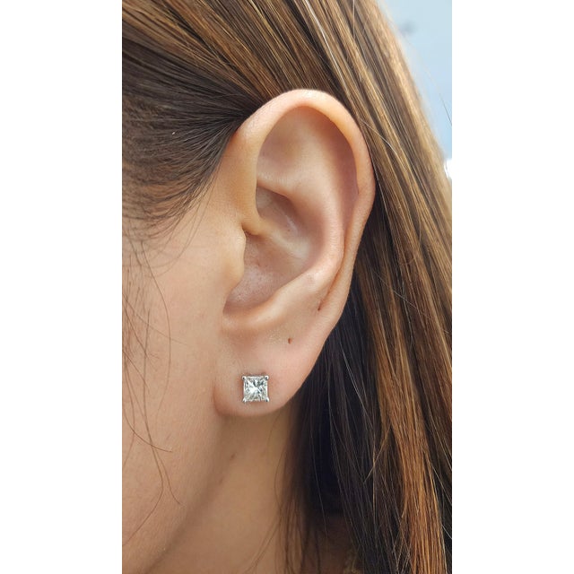 A pair of modern 14K white gold stud earrings featuring approximately 1.00 carat of natural princess-cut white diamonds,...