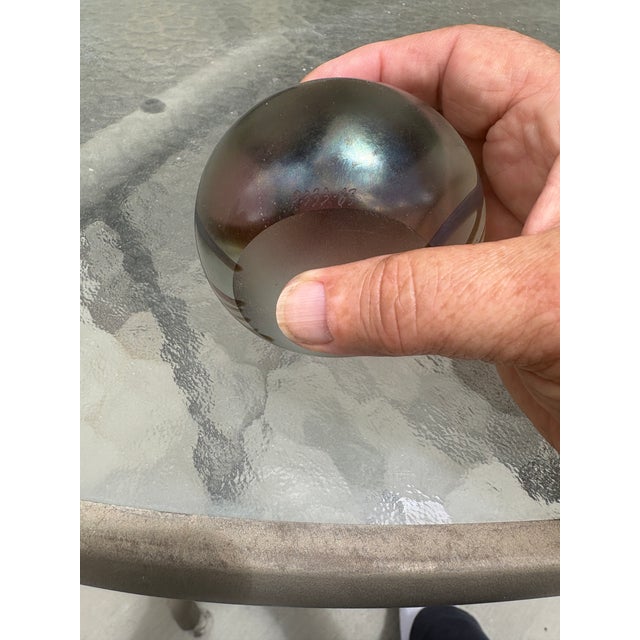 This art glass piece is an iridescent hand-blown paperweight crafted by the artist Roger Roland in 1983. It features a...