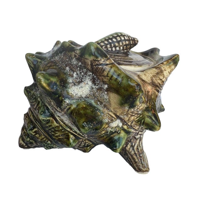 This ceramic conch shell dish features a sculptural, textured design with an earthy glaze in shades of brown, green, and...