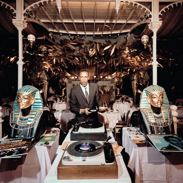 Slim And Sphinx by Slim Aarons circa 1964: New York DJ Slim Hyatt at work in Shepheard’s night club whose decor recreates...