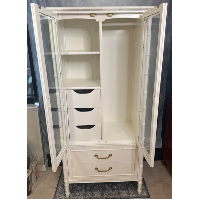 White Thomasville Allegro faux bamboo armoire features brass hardware. Freshly painted white, this cabinet has glass doors...