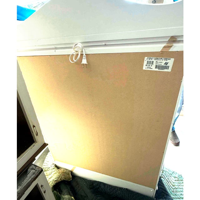 A charming white lighted display cabinet by Stanley Furniture Company, featuring oval glass doors, interior shelving, and...