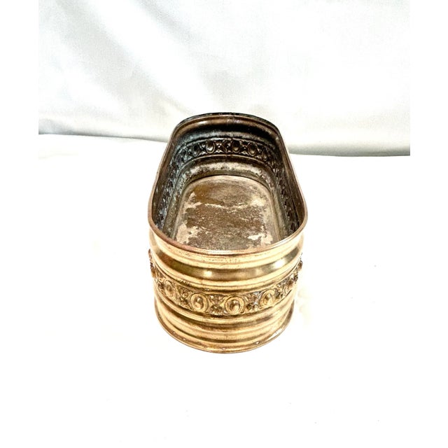 A charming oval brass cachepot featuring an embossed floral band and warm polished brass finish. Its low elongated shape...