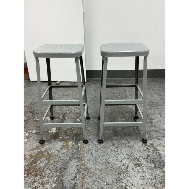 Design Plus Gallery presents a Pair of Vintage Lyon Workspace Model 1901 Industrial Barstools. Each stool has a perforated...