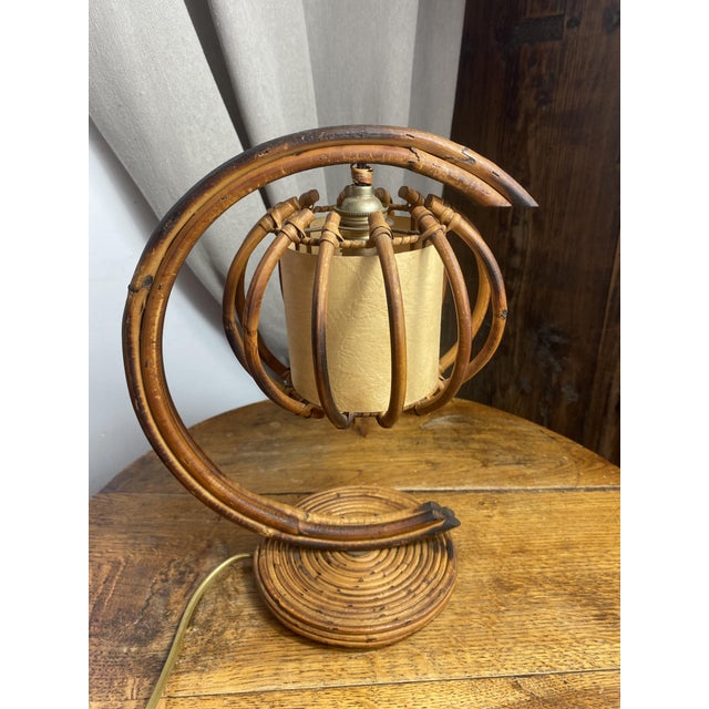 A 1960s rattan and bamboo table lamp by Louis Sognot, distinguished by its arched structure and suspended cage-shaped...