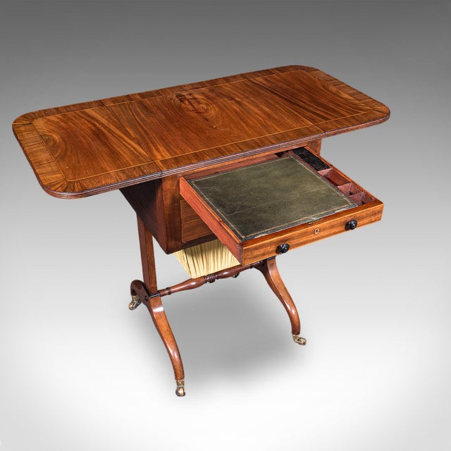 This is an antique drop leaf ladies work table. An English, mahogany sewing or writing table, dating to the Regency...