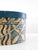 Vintage mid-century hat box featuring a round form, blue and tan graphic paper design, matching lid, and braided cord...