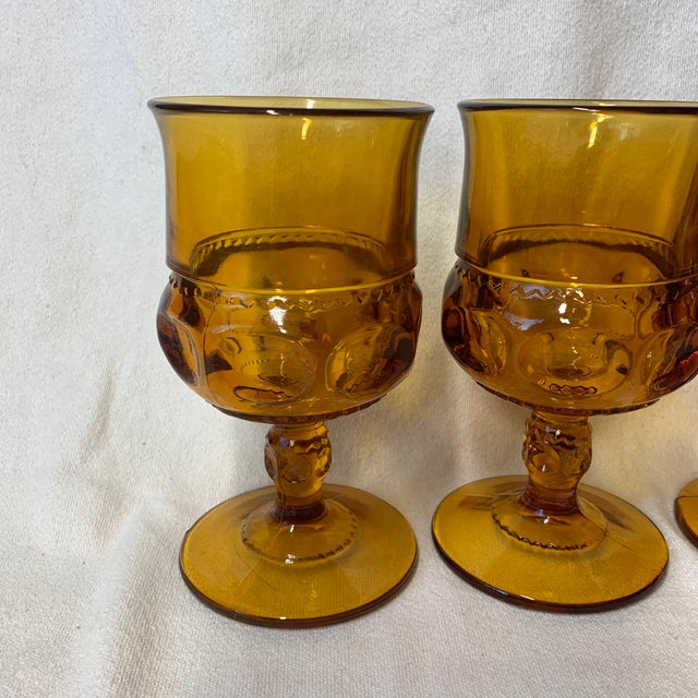 This vintage Indiana Glass amber footed goblet features a classic King's Crown thumbprint pattern and a textured stem.
