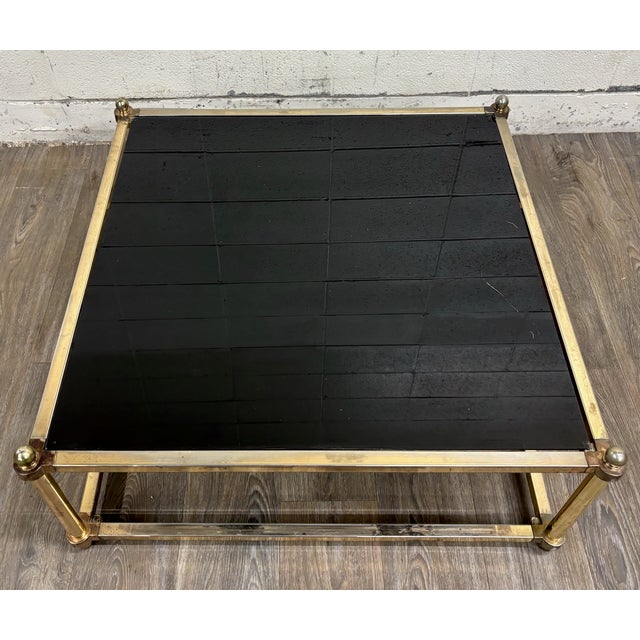 This is a stunning vintage Maison Jansen style Hollywood Regency coffee table featuring a brass-tone metal frame, smoked...