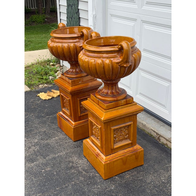 A striking pair of large-scale campana-form garden urns, each set atop a matching square plinth pedestal, finished in a...