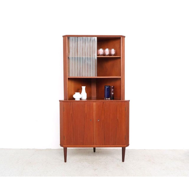 Vintage Danish corner cabinet with display case from the 1960s, made of teak veneer. The cupboard combines closed storage...