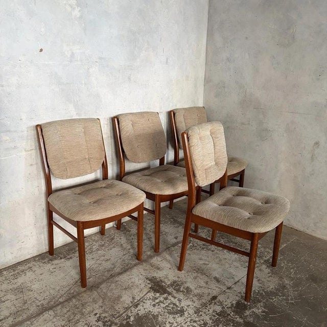 A matching set of four Nathan Furniture dining chairs with warm teak-toned frames and comfortably padded beige button-...