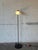 This minimalist floor lamp features an adjustable conical shade mounted on a slim metal standard. The sleek silhouette...