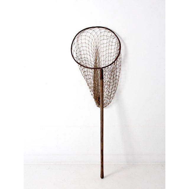 This early 20th century fishing net features a hand-forged bent iron hoop, hand-tied cotton netting, and a worn wooden...