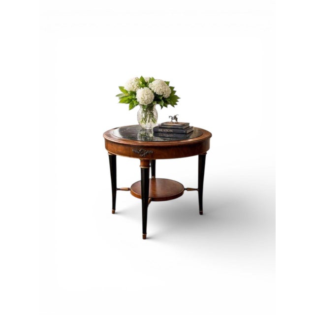 Elegant, antique round accent table featuring a black marble insect top, warm, honey, toned, wood, apron, and contrasting...