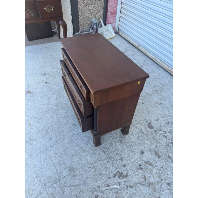 Elegant Italian Empire-style nightstand featuring a warm walnut-toned wood finish, three paneled drawers, and distinctive...