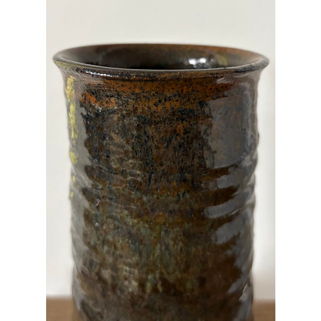 A sculptural vintage studio pottery vase with a tall cylindrical form and richly layered earth-tone glaze. Hand-thrown in...