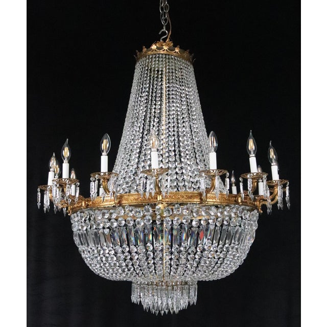 Empire style basket crystal chandelier with an ornate brass frame. This light requires twenty-four E-12 candelabra light...