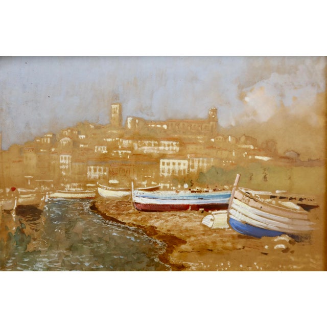 An atmospheric and evocative harbor scene depicting beached fishing boats on the shore with a hilltop village rising...