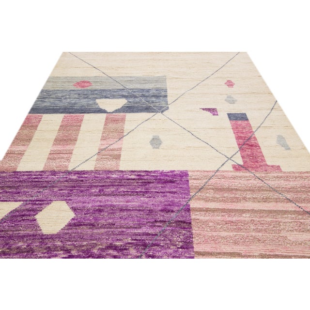 This modern handmade wool rug features a beige and purple field with an allover tribal design. This rug measures 7'2" x 10'.