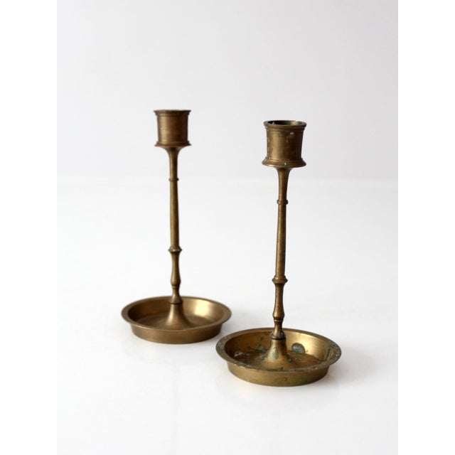 Pair of mid-century brass candlesticks featuring slender turned stems, engraved floral drip pans, and a warm aged patina....
