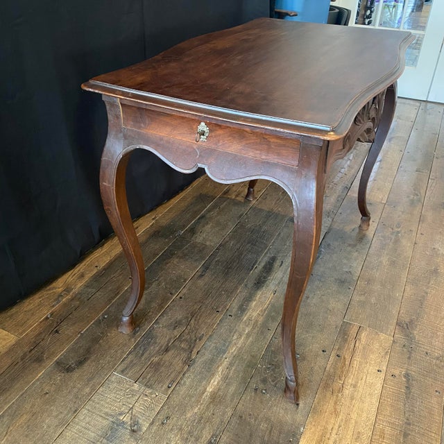 Elegant 19th century French walnut side table or desk featuring a gracefully curving rectangular top above a deeply carved...