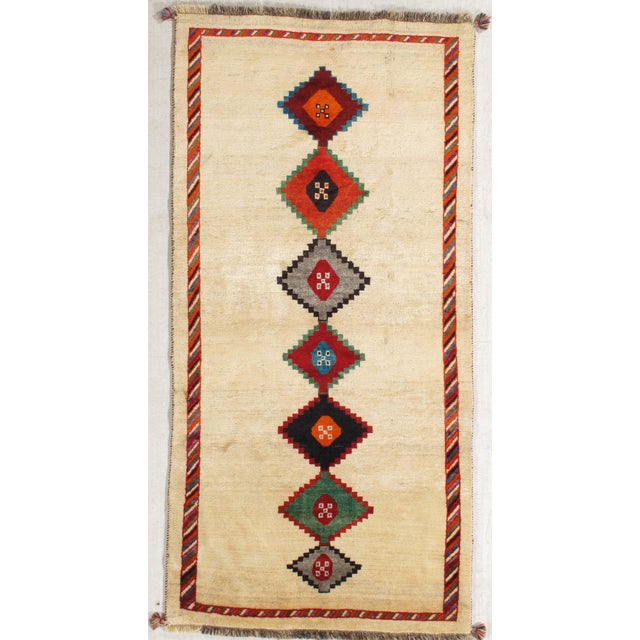 Vintage Persian Gabbeh hand-knotted wool rug featuring an ivory field with a vertical row of colorful stepped diamond...