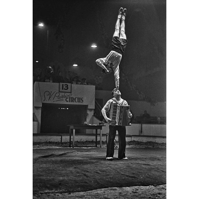 S V Parkin's Circus Acrobats An acrobat performs a handstand on one arm, which balances on the head of an accordionist,...
