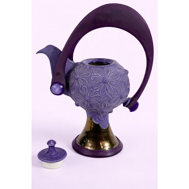 This stunning decorative teapot features a soft lavender body adorned with intricate raised floral patterns, giving it a...