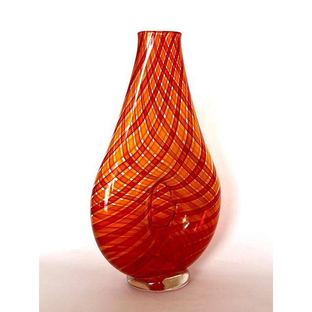 The handblown glass bottle in a tall, flattened, tapering shape with gently flared mouth and rounded lower body is...