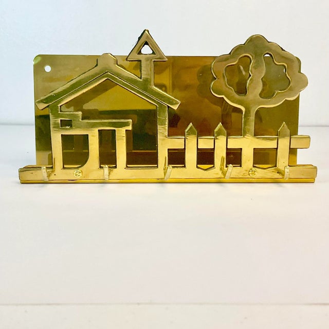 This is a delightful brass wall-mounted key hook and letter/mail holder. It features an American household scene with a...