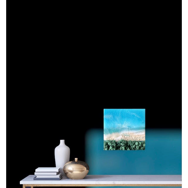 This mixed media piece captures the serene essence of a beach scene, where vibrant turquoise waters meet a sandy shore....