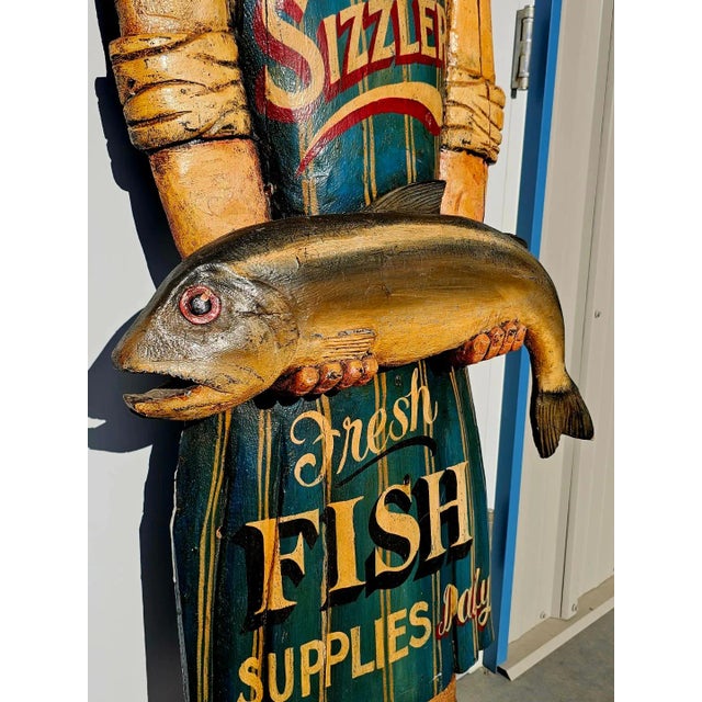 Vintage Mid-century Sizzler wooden sign. It depicts a fishmonger holding a large fish. The carved wooden sign is in good...