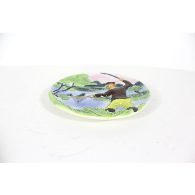This is a vintage ceramic pottery wall hanging plate, hand-painted, with raised detail, showcasing a fishing scene.. This...