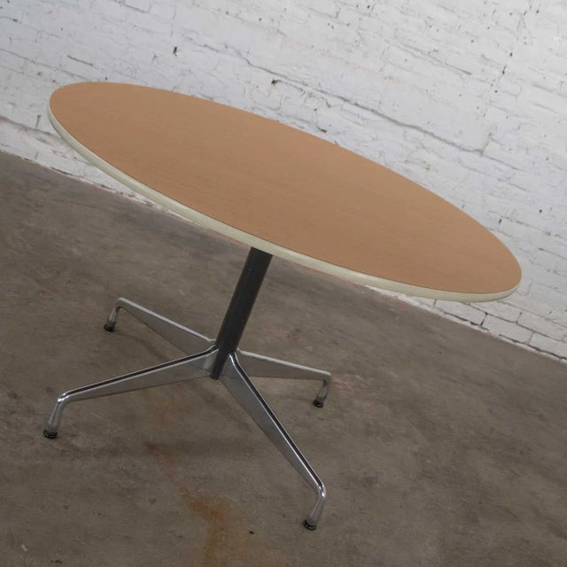Renowned Eames Herman Miller round table with the universal base and a wood grain laminate top with off white edge trim,...