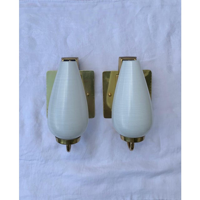 A stylish pair of 1950s Italian Stilnovo style single light brass with original white spun glass shades and black...