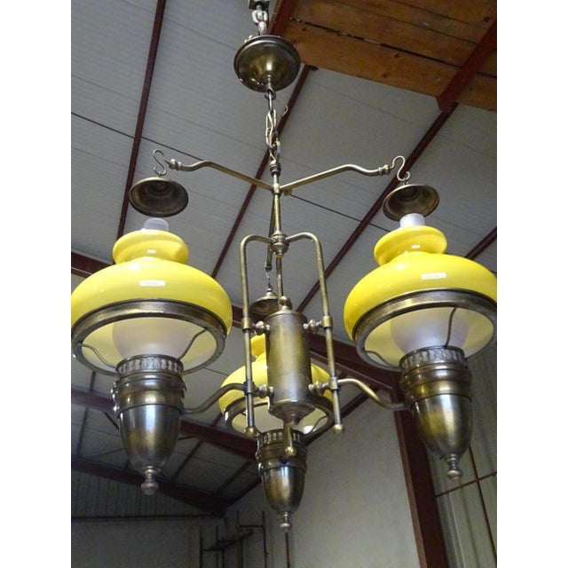 Complete chandelier from the 1970s, with an imposing brass frame, three frosted white glass shades shaped like oil lamps,...