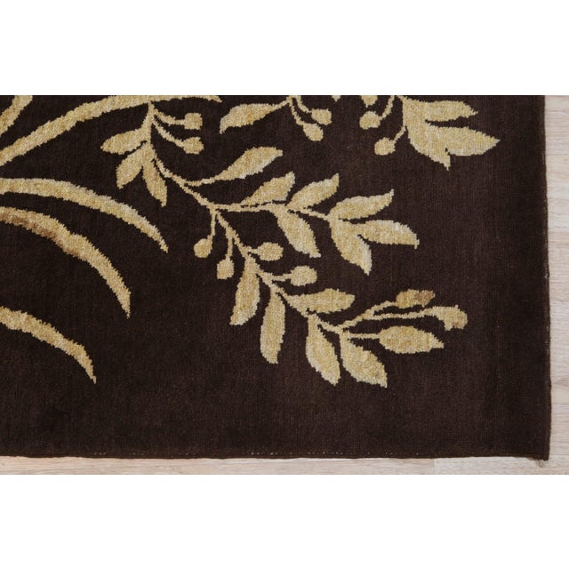 A 10' x 14' hand-knotted wool rug with a chocolate brown ground with large ivory botanical sprays and vines, in a low,...