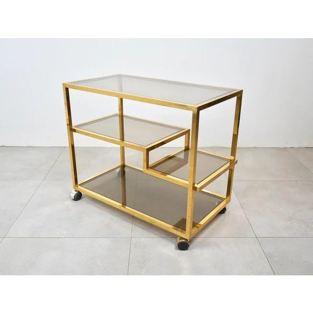 This vintage brass and smoked glass serving cart features unique midcentury design, combining simple lines and plenty of...
